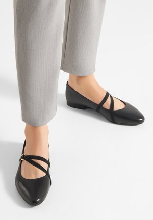 Bailarinas de cuero negro con punta puntiaguda, con dos tiras cruzadas y un pequeño tacón. Combinadas con pantalones a medida gris.