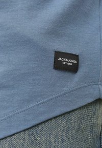 Blå bomulds T-shirt med rund hals og korte ærmer, med et sort mærke som viser "JACK & JONES EST. 1990" syet på siden.