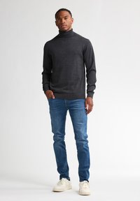 Suéter de cuello alto gris oscuro en tejido de punto suave, combinado con unos jeans ajustados azules y zapatillas blancas. Diseño sencillo y casual con una textura suave.