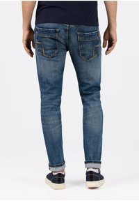 Schmal geschnittene blaue Denim-Jeans mit Kontrastnähten, zwei Gesäßtaschen und umgeschlagenem Saum. Die Textur wirkt glatt mit leichtem Verblassen.