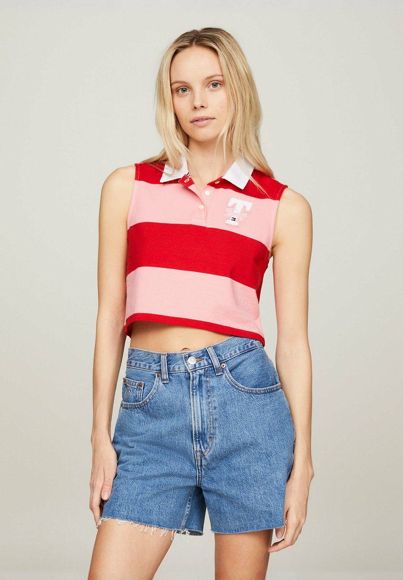 Rød og lyserød stribet ærmeløs poloshirt med hvid krave og logo, parret med højtaljede denimshorts med frynsede kanter.