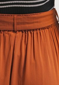 Terracotta nederdel med samlet stof i taljen, der har et elastisk bånd og en glat tekstur. Stribet sort og hvid top ovenfor.