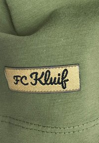 Olijfgroene beanie met een geribbelde textuur, met een rechthoekig gouden label waarop "FC Kluif" in het zwart geborduurd is.
