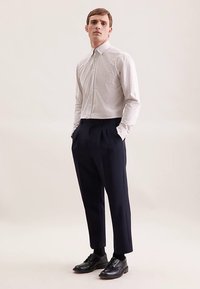 Camicia a maniche lunghe a quadri bianchi e blu abbinata a pantaloni navy plissettati e scarpe nere. Design solido e classico con vestibilità sartoriale.