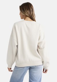 Sudadera de color crema, de corte oversize, con dobladillo y puños acanalados. Material de suave mezcla de algodón, con un pequeño parche en el centro de la parte trasera.