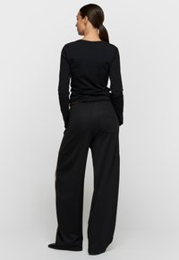 Top negro de manga larga combinado con pantalones anchos negros; textura suave, diseño minimalista, con un bolsillo trasero y aberturas laterales en los pantalones.