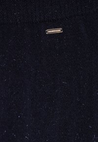 Marineblauer Strickpullover mit einer weichen Textur und einem metallischen Etikett mit der Aufschrift "DRIKMASTER" auf der Vorderseite. Zarte glänzende Akzente im gesamten Stoff.