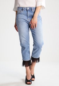 Světle modré džíny ve zkrácené délce s třepeným lemem, které mají černou tylovou vrstvu na manžetách, v kombinaci s černými otevřenými lodičkami.