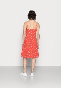 Rotes Blumenkleid mit dünnen Trägern, midi-länge und ausgestellter Silhouette. Hergestellt aus leichtem Stoff, mit kleinen weißen und lila Blumen.