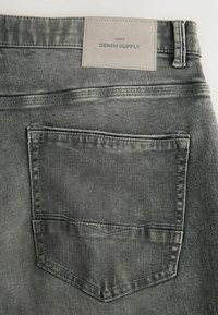 Gray denim jeans with a textured finish, featuring a back pocket and a gray label titled "DENIM SUPPLY" stitched at the waistband.