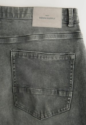 Sivé deninové nohavice s textúrovaným povrchom, so zadnou vreckom a sivou nášivkou s názvom "DENIM SUPPLY" pri páse.