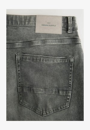 Sivé deninové nohavice s textúrovaným povrchom, so zadnou vreckom a sivou nášivkou s názvom "DENIM SUPPLY" pri páse.