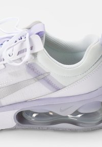 Zapatilla deportiva blanca y lavanda con parte superior de malla, collar acolchado y amortiguación de aire transparente. Presenta un logo de Nike en plata en el lado.
