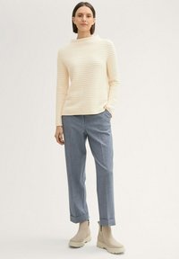 Pull crème à rayures avec un col haut, associé à un pantalon tailleur gris clair et des bottines beige. Texture lisse sur l'ensemble.