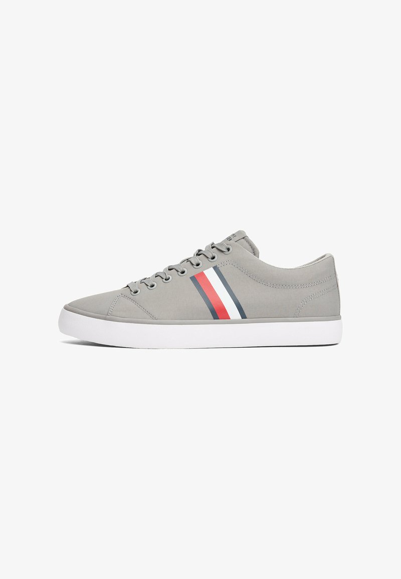 Grå lærreds sneakers med lavt design, præget af en hvid gummisål og røde, hvide og marineblå stribede detaljer på siden.