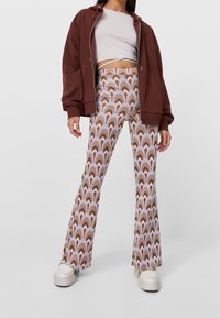Uitlopende broeken in een meerkleuren golfpatroon van bruin, crème en lavendel. Gecombineerd met een cropped grijze top en een bruin ritsjack.