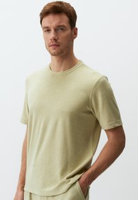 Jasnozielona, krótko rękawowa koszulka z miękkiego materiału. Posiada okrągły dekolt i luźny krój, z subtelnymi detalami szycia wzdłuż szwów.