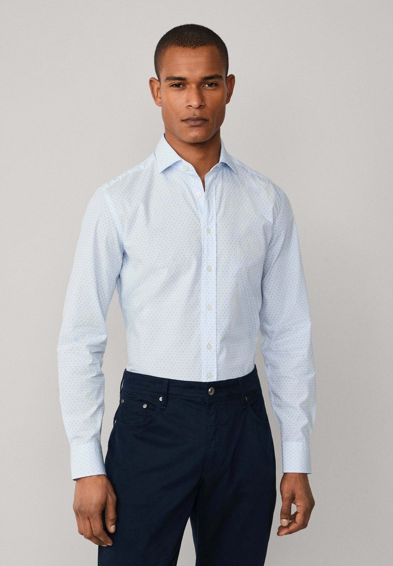 Camicia button-up azzurro chiaro con piccoli pois navy, con colletto alla francese e maniche lunghe, abbinata a pantaloni navy scuri.