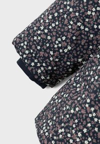 Stoff mit floralem Muster in Marineblau, verziert mit kleinen weißen und rosa Blumen. Geripptes Marineblau am Ärmel für zusätzliche Textur.