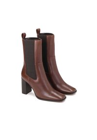 Botas de cuero marrón hasta el tobillo con puntera cuadrada y paneles laterales elásticos. Presentan un tacón cuadrado y lengüetas en la parte superior para facilitar su uso.