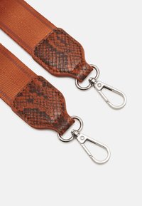 Säädettävä hihna, jossa oranssia tekstiilimateriaalia ja ruskeat käärmekuvioiset nahkaosat, ja metallikiinnikkeet kiinnittämistä varten.