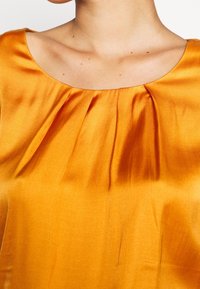 Satin orange Top mit runder Ausschnitt, gerafften Falten an der Vorderseite und glatter Textur.