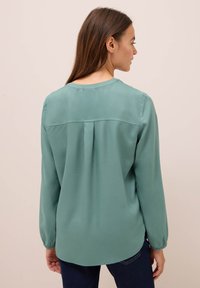 Türkosa långärmad blus med rundad halsringning, bakfåll och elastiska muddar, i en mjuk och lättviktig tyg.