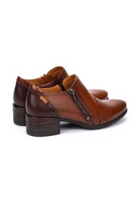 Bottes de cheville en cuir marron avec une fermeture éclair sur le côté, bout arrondi et petit talon carré, présentant des accents en cuir plus foncé et des détails de couture contrastants.
