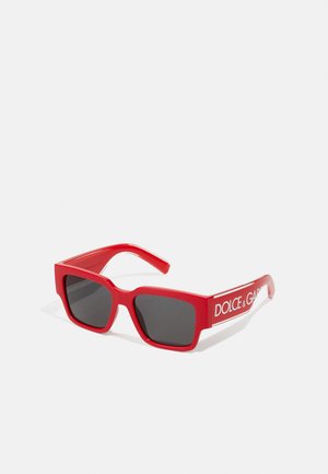 Óculos de sol vermelhos de plástico com armações quadradas, lentes pretas e detalhes em logotipo branco nas hastes. Design elegante com acabamento brilhante.