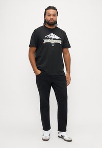 Μαύρο κοντομάνικο μπλουζάκι με λευκό γραφικό βουνού και το κείμενο «Jack & Jones», συνδυασμένο με μαύρο παντελόνι και λευκά αθλητικά παπούτσια.