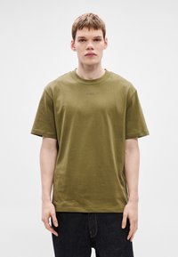 Bombažna majica olivno zelene barve z okroglim izrezom in kratkimi rokavi. Ima subtilen logotip na sredini prsnega koša ter sproščen kroj.