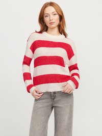 Pull à rayures rouges et blanches avec une coupe décontractée, texture tricotée, col rond et manches longues, associé à un jean gris clair.