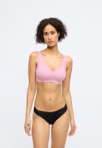 Bralette rose clair avec des bretelles larges et un décolleté en V profond, associé à des panties noirs ornés de dentelle et à taille basse.