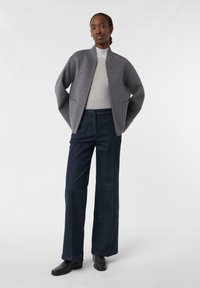 Giubbotto bomber grigio in lana con chiusura a zip e tasche laterali, abbinato a pantaloni in denim a gamba larga blu scuro e stivaletti neri.