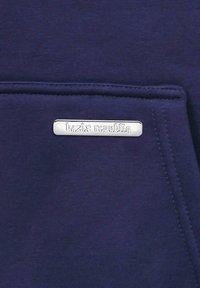 Un tissu de sweat-shirt bleu marine avec une petite étiquette en argent gravée, mettant en valeur une texture lisse et des lignes épurées.
