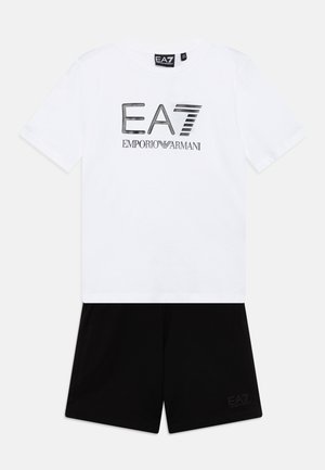 T-shirt blanc à manches courtes avec un logo EA7 noir, associé à un short noir portant une petite imprimé EA7 sur la jambe, fabriqué en coton lisse.