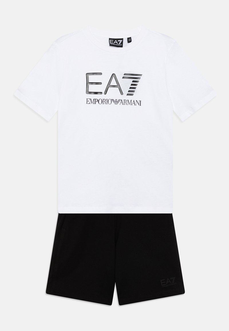 Camiseta blanca de manga corta con un logo EA7 negro, combinada con pantalones cortos negros que tienen una pequeña impresión EA7 en la pierna, hechos de un suave material de algodón.