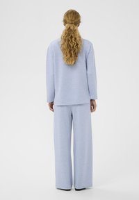 Hele sinine pusa ja laia säärega püksid, mis on valmistatud pehmest ja tekstuurse kangaga; lahtine lõige; minimalistlik disain ilma nähtavate logode või dekoratsioonideta.