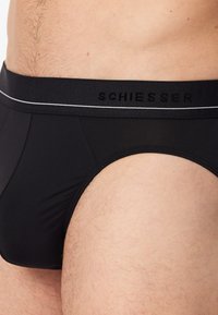 Slip neri realizzati in tessuto elasticizzato, caratterizzati da una cintura ampia con un logo discreto e dettagli in cucitura bianca. Texture liscia.