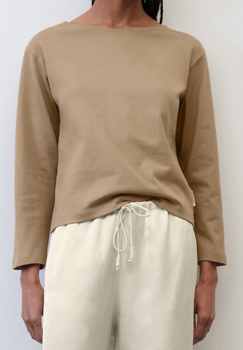 Langarmshirt mit Rundhalsausschnitt aus hellbrauner Baumwolle. Weiche Textur mit lockerer Passform, kombiniert mit beigen Jogginghosen mit Kordelzug für zusätzlichen Komfort.