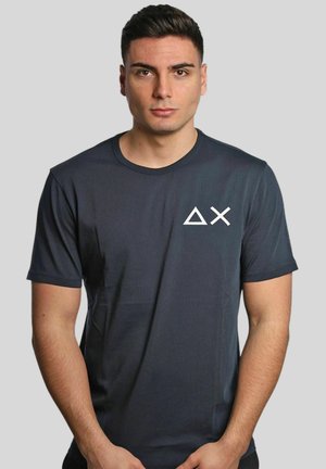 T-shirt corto grigio scuro realizzato in un tessuto liscio, con un logo geometrico bianco sul lato sinistro del petto. Design classico con collo a giro.