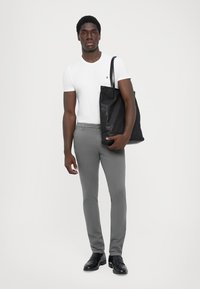 T-shirt bianco aderente, pantaloni grigi slim-fit, scarpe in pelle nera e una grande borsa tote nera. Texture lisce e design minimalista.