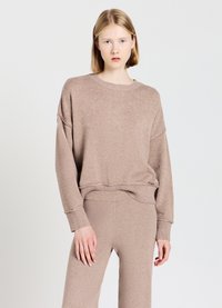 Maglione beige lavorato a maglia con scollatura rotonda, spalle scese e polsini a coste. Abbinato a pantaloni beige coordinati, caratterizzati da un design senza cuciture.