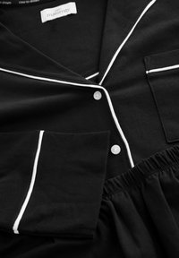 Black maternity pajama top and pants with white piping, button closure, chest pocket, and elastic waistband, folded flat.