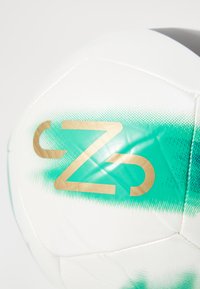 Biała piłka nożna z zielonym gradientowym wzorem i złotym logo "Z". Teksturowana powierzchnia z szytymi panelami, odpowiednia do gry na zewnątrz.