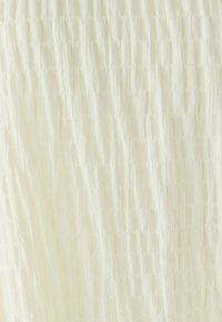 Tessuto testurizzato di colore bianco sporco con un motivo stropicciato, che suggerisce morbidezza e leggerezza. Ideale per abbigliamento o biancheria da letto.