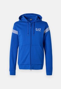 Blue zip-up hoodie with a hood, featuring a white EA7 logo, two front pockets, and striped accents on the sleeves. Soft fabric texture.