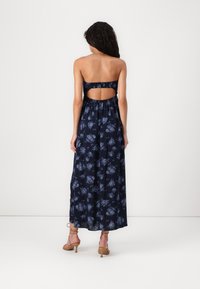 Navy floral maxi dress with a strapless design and open back. Features a flowing silhouette and textured fabric with blue flower patterns.