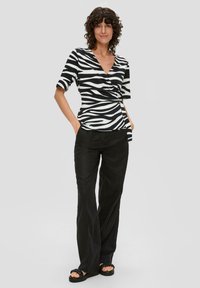 Zwart-witte zebraprint top met een V-hals en korte mouwen, gecombineerd met losse zwarte broeken en zwarte platform sandalen.