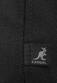 Tessuto nero con una trama diagonale, caratterizzato da un'etichetta grigia Kangol con il logo di un canguro. Il materiale sembra resistente e strutturato.